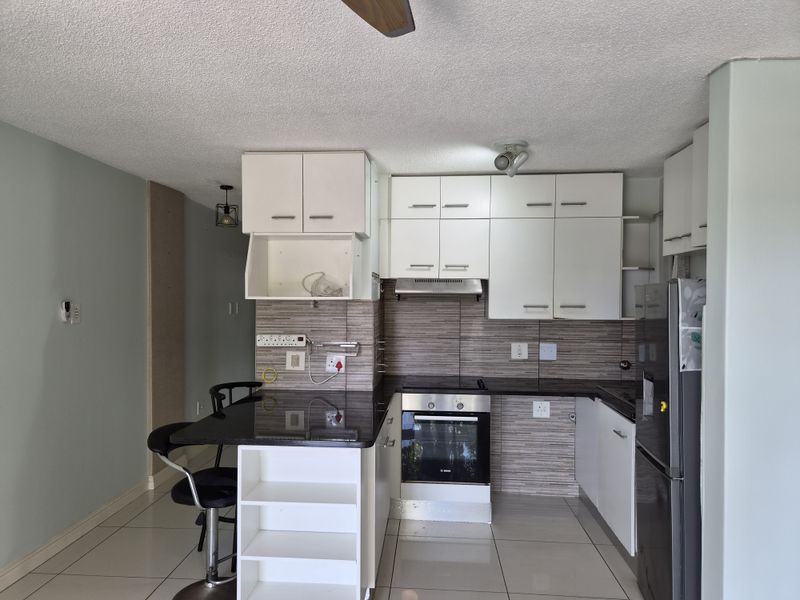 Compact kitchen featuring white cabinetry, dark laminate countertops, built-in oven and hob, tiled backsplash, and a functional breakfast bar area.