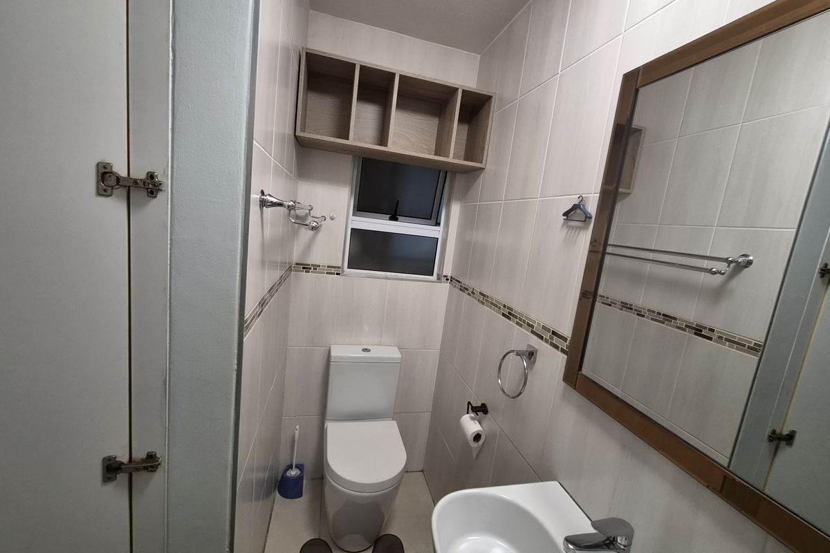 A compact, well-maintained bathroom featuring tiled walls, a modern toilet, a wall-mounted basin, and overhead storage cabinetry.