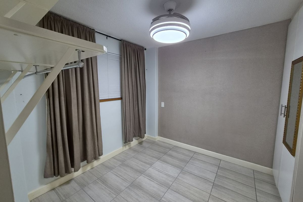 A clean, empty bedroom featuring modern tiled flooring, a ceiling fan, and a built-in wardrobe with neutral wall finishes.
