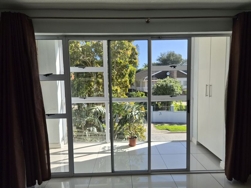 Bright living area featuring large sliding glass doors that open to an outdoor space, complemented by neutral tiled flooring and built-in storage cupboards.