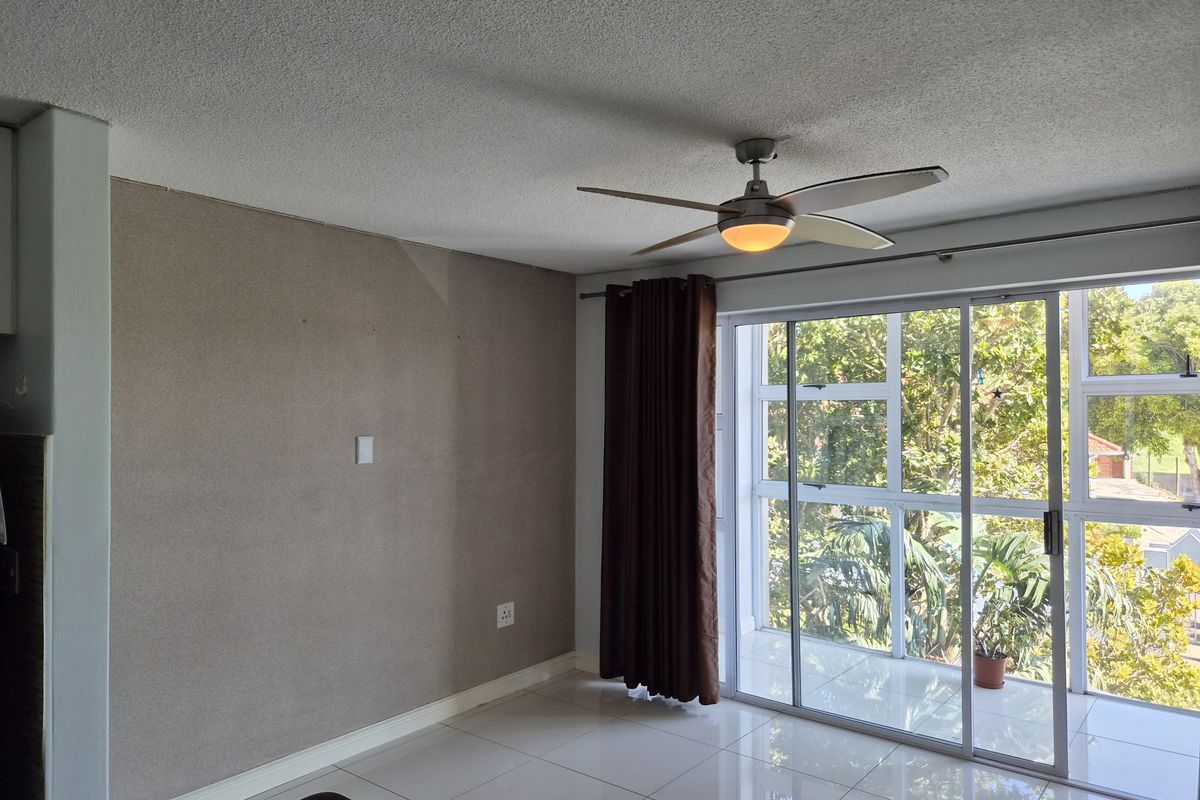 A bright, empty living area featuring tiled floors, a ceiling fan, and large sliding glass doors leading to an outdoor balcony.
