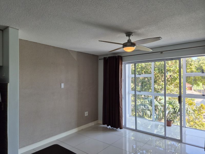 A bright, empty living area featuring tiled floors, a ceiling fan, and large sliding glass doors leading to an outdoor balcony.