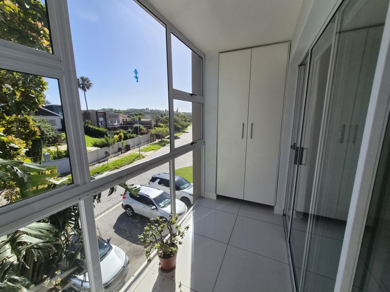 Enclosed balcony featuring tiled flooring, built-in storage cupboards, and large aluminium-framed windows offering an elevated street view.