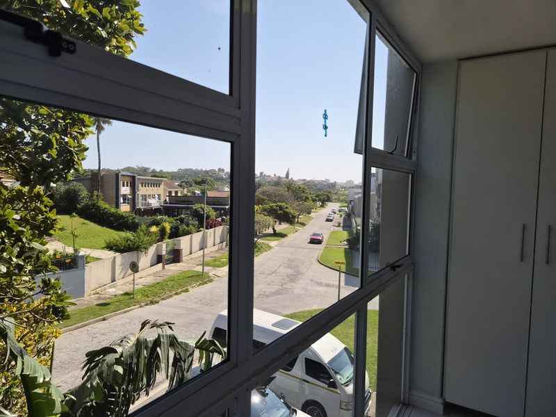 An enclosed balcony area featuring aluminium window frames and built-in storage cupboards, offering a clear view of the surrounding street and neighbourhood.