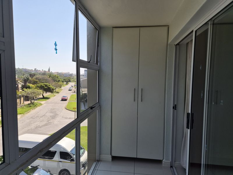Enclosed balcony featuring tiled flooring, aluminium window frames, and a convenient built-in storage cupboard, offering views of the street.