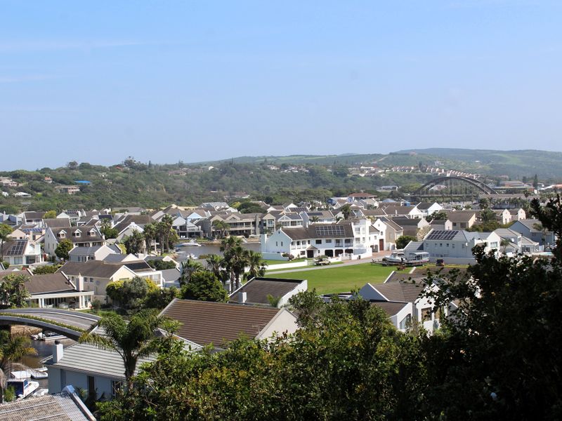 An elevated panoramic view overlooking a residential estate, featuring coastal architecture, green spaces, and a bridge in the distance.