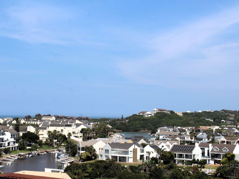 An elevated panoramic view of a coastal residential estate featuring multiple homes, lush greenery, and a scenic waterway.