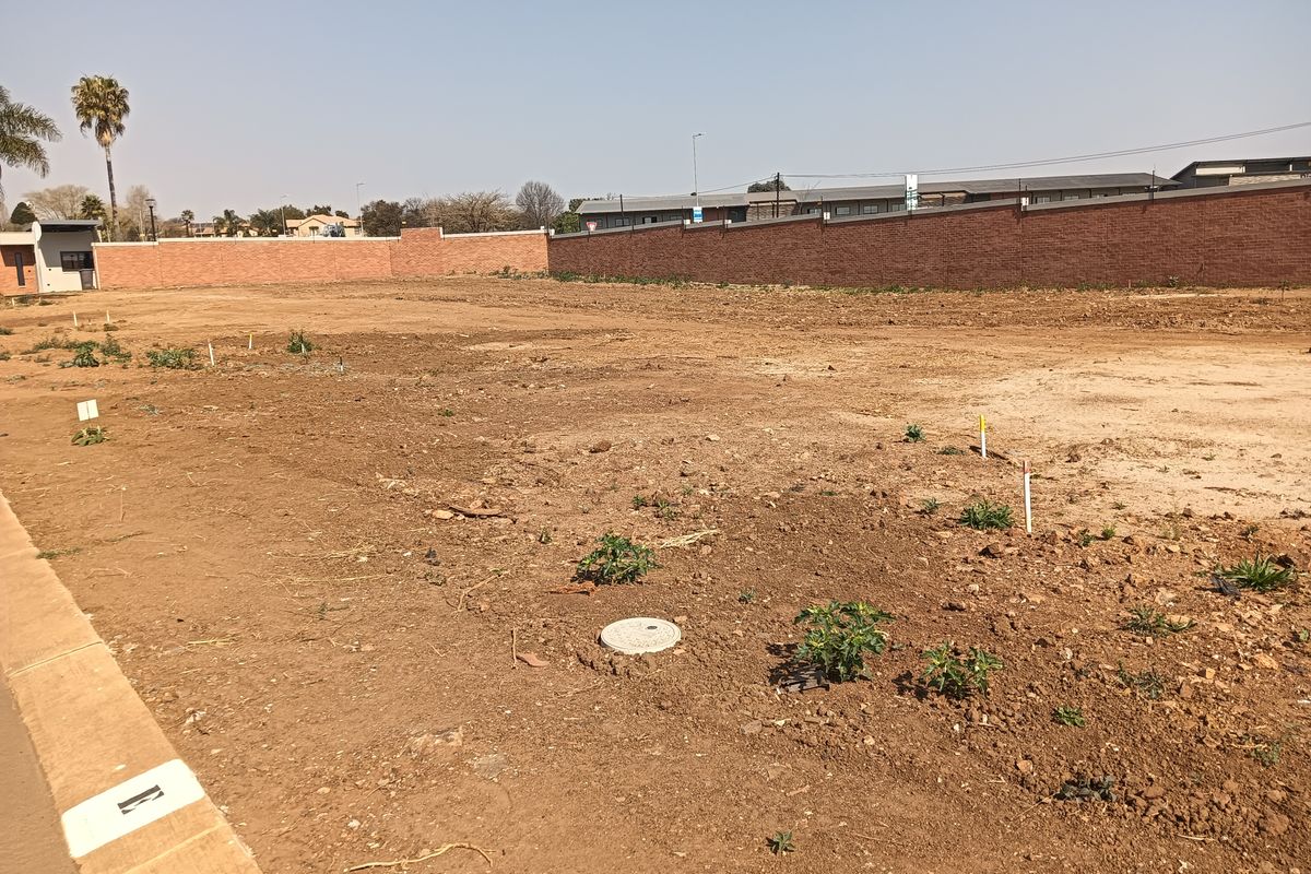 A vacant residential plot featuring a perimeter brick wall, survey markers, and utility access points, ready for development.