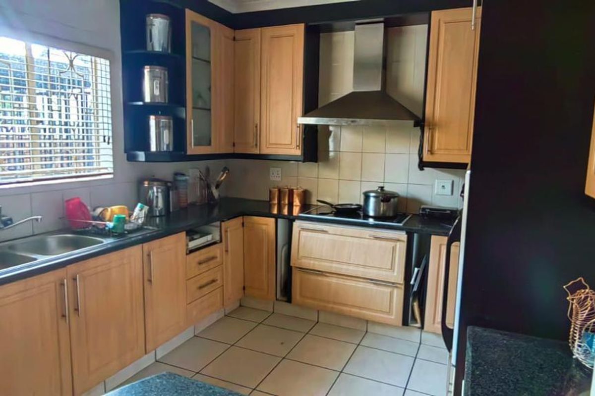 Functional kitchen featuring wooden cabinetry, dark countertops, a stainless steel extractor fan, and a double bowl sink with a window view.