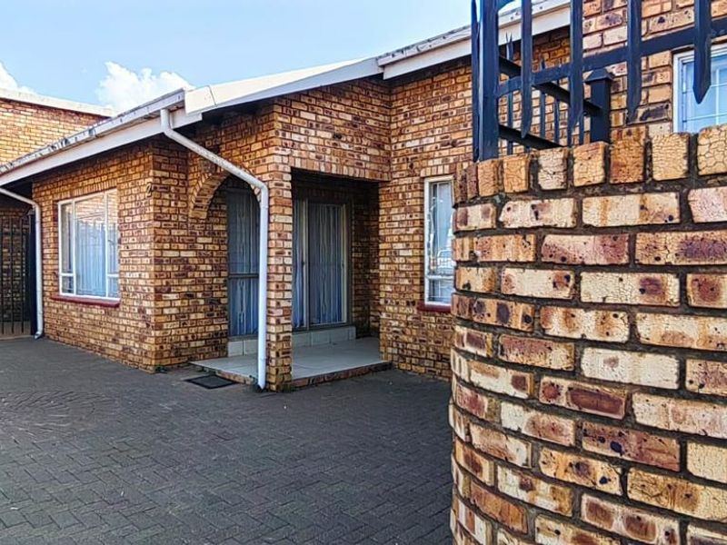 Front exterior view of a face brick house featuring a paved driveway, security gate, and metal window frames.