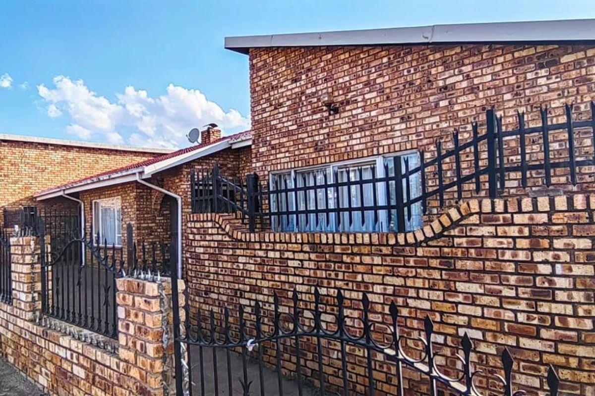 A front exterior view of a face brick house featuring secure wrought iron perimeter fencing and a gated entrance.