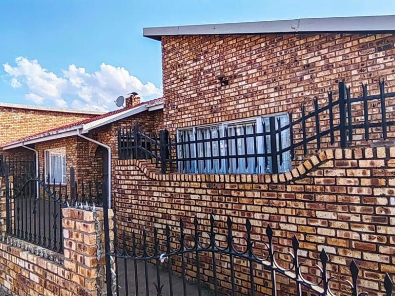 A front exterior view of a face brick house featuring secure wrought iron perimeter fencing and a gated entrance.