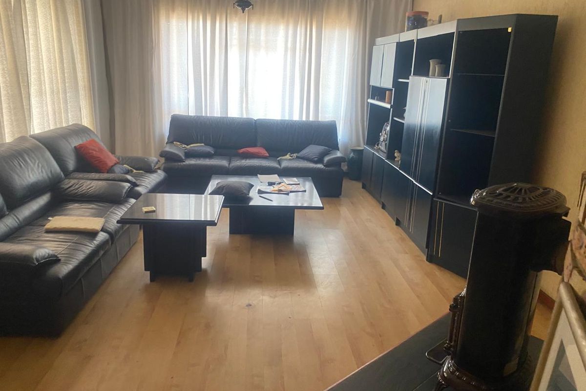 A living room featuring laminate flooring, a freestanding fireplace, and large windows with curtains, providing a functional and comfortable living space.