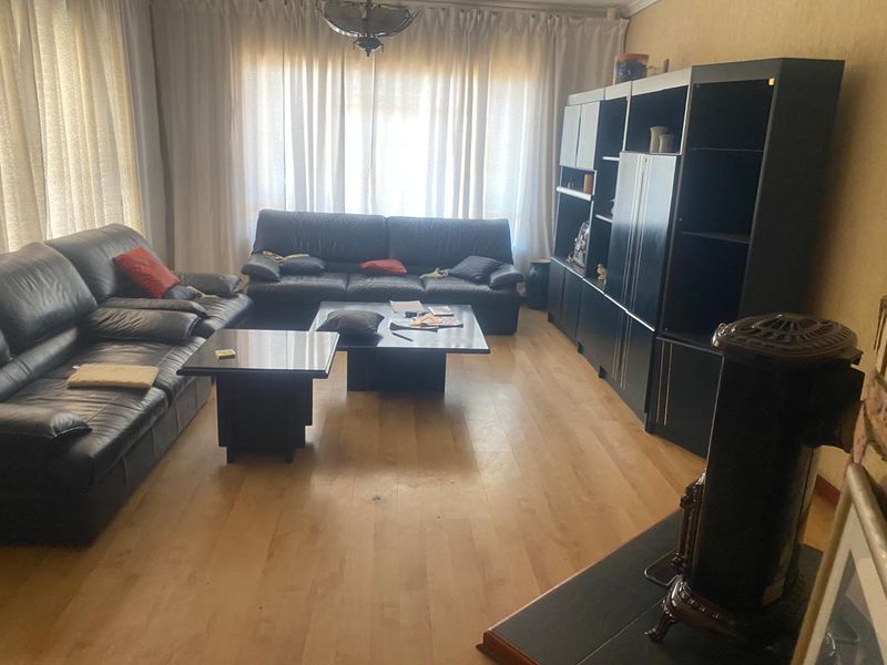 A living room featuring laminate flooring, a freestanding fireplace, and large windows with curtains, providing a functional and comfortable living space.
