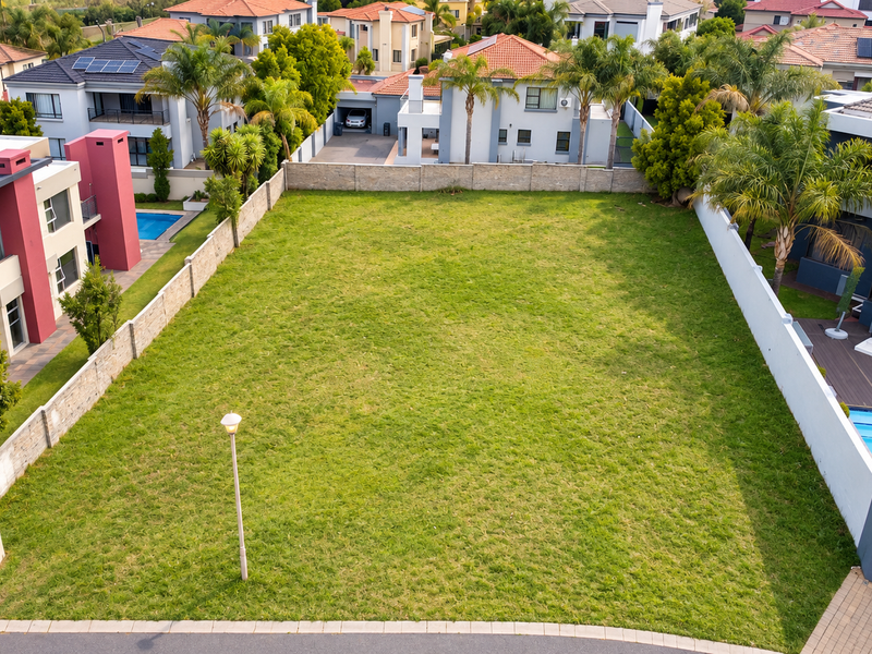 An aerial view of a vacant residential plot featuring a well-maintained grass lawn and perimeter walling, situated within an established residential estate.