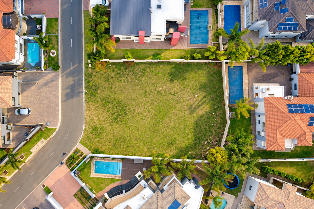 An aerial view of a vacant residential plot situated within a developed neighborhood, featuring clear boundary lines and surrounding residential properties.