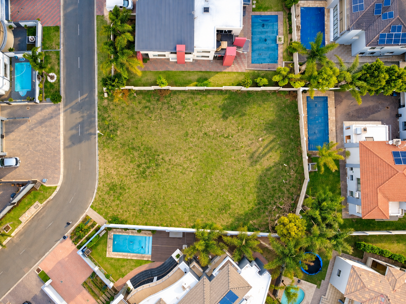 An aerial view of a vacant residential plot situated within a developed neighborhood, featuring clear boundary lines and surrounding residential properties.