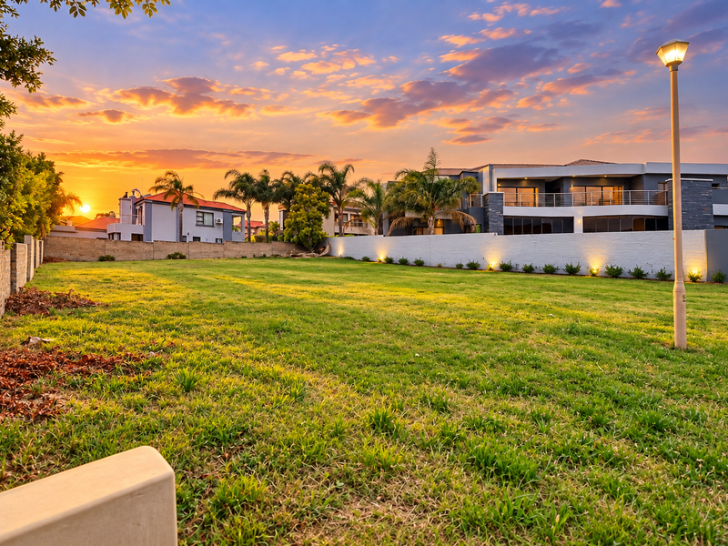 A spacious, well-maintained residential plot featuring a manicured lawn, perimeter boundary walls, and integrated garden lighting at sunset.