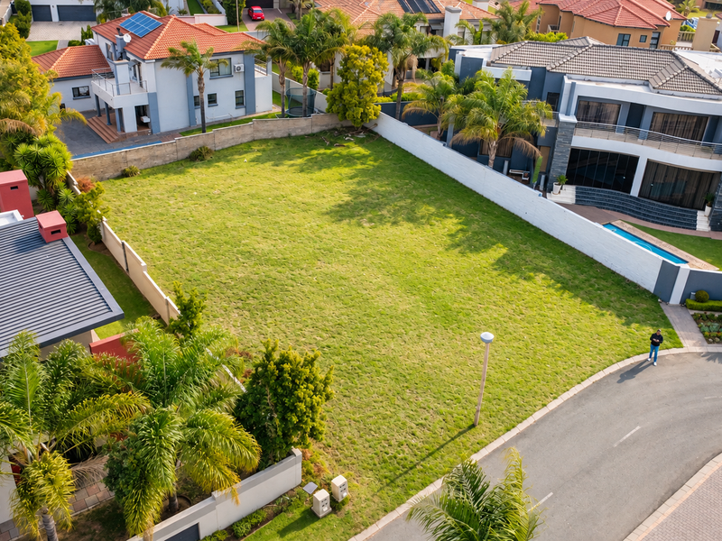 An elevated aerial view of a vacant residential plot situated within a developed estate, featuring established boundary walls and street access.