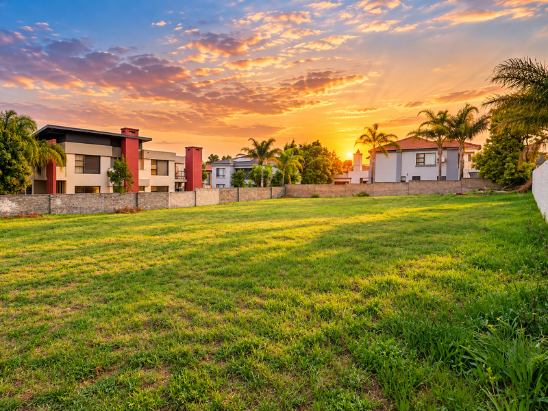 A spacious, level residential vacant plot featuring a well-maintained lawn and secure boundary walls, set against a scenic sunset backdrop.