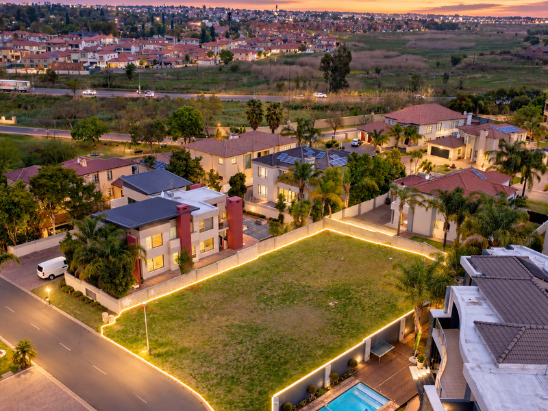 An elevated aerial view of a vacant residential plot in a developed estate, featuring perimeter lighting and established surrounding residential infrastructure.