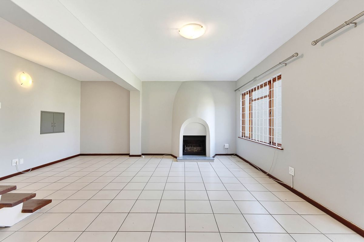 Spacious, empty living room featuring tiled flooring, a unique built-in fireplace, and large windows with security bars.