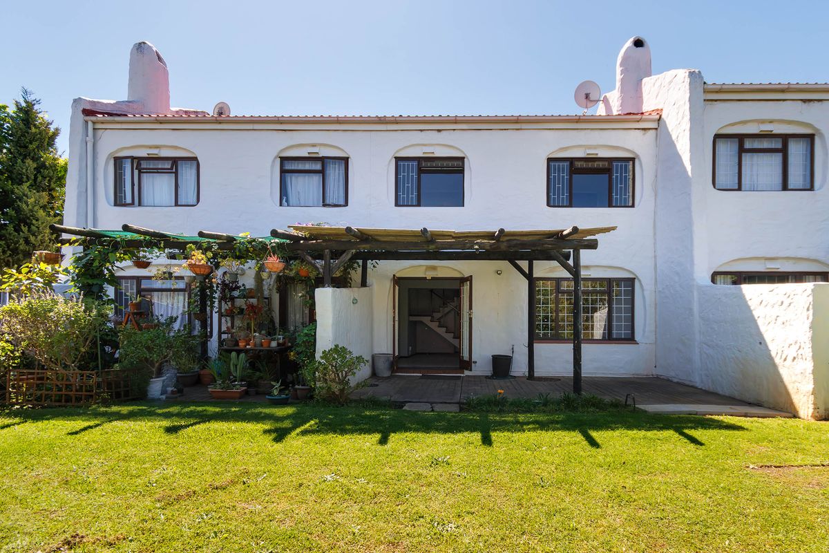 Rear elevation of a townhouse featuring a timber pergola over a wooden deck, established garden, and traditional white-painted facade with chimney stacks.