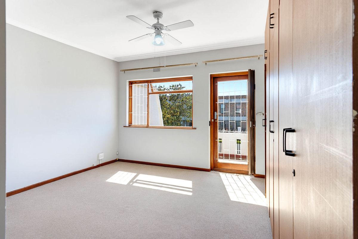 A bright, empty bedroom featuring built-in cupboards, a ceiling fan, and direct access to an outdoor area through a secure door.