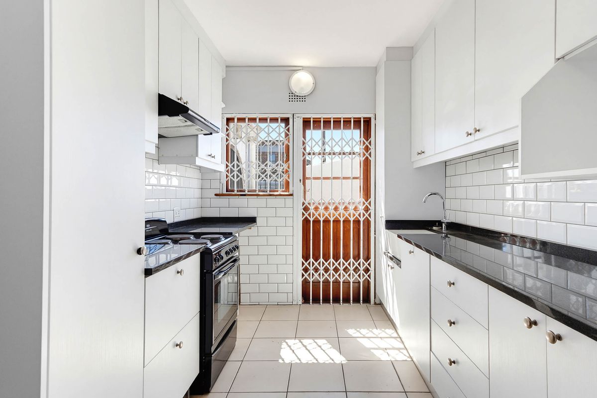 A clean, galley-style kitchen featuring white cabinetry, black granite countertops, subway tile backsplash, and a security gate leading to the exterior.