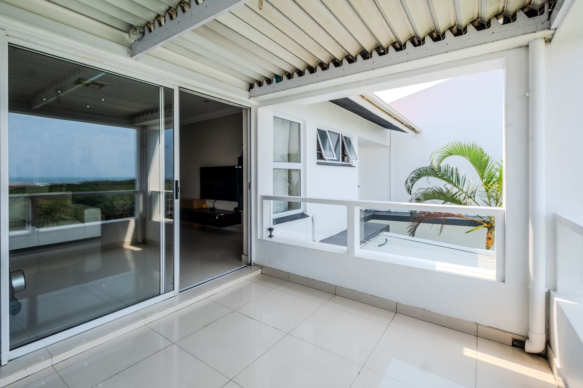 A covered balcony featuring tiled flooring, sliding glass doors, and a protective railing, offering a functional outdoor space with views.