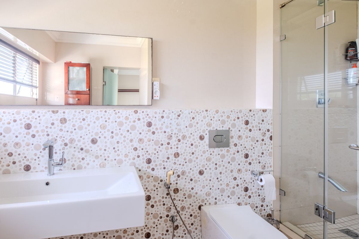 Modern bathroom featuring a wall-mounted basin, wall-hung toilet with flush plate, and a glass-enclosed shower with decorative mosaic-style wall tiling.