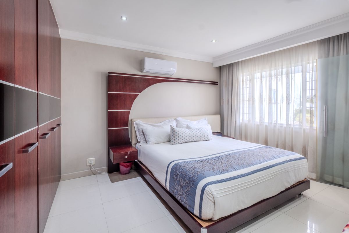 A well-maintained bedroom featuring tiled flooring, built-in cupboards, an integrated air conditioning unit, and recessed lighting with large windows.