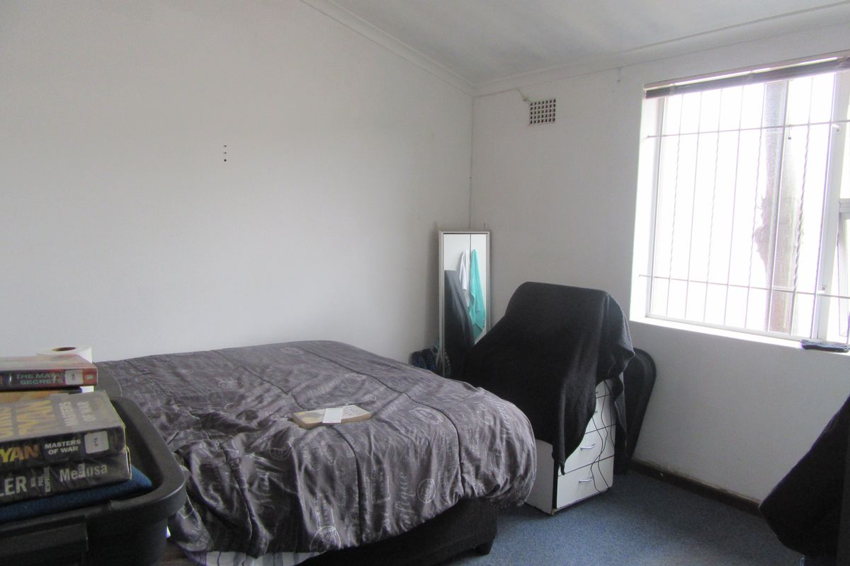 A bedroom featuring a window with security bars and a ventilation grille, requiring cosmetic updates to the wall finishes and flooring.