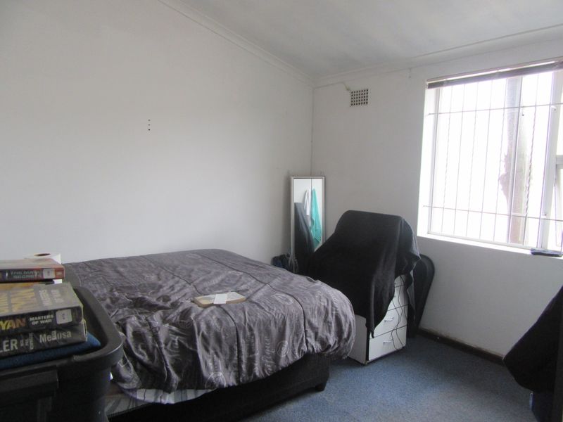 A bedroom featuring a window with security bars and a ventilation grille, requiring cosmetic updates to the wall finishes and flooring.