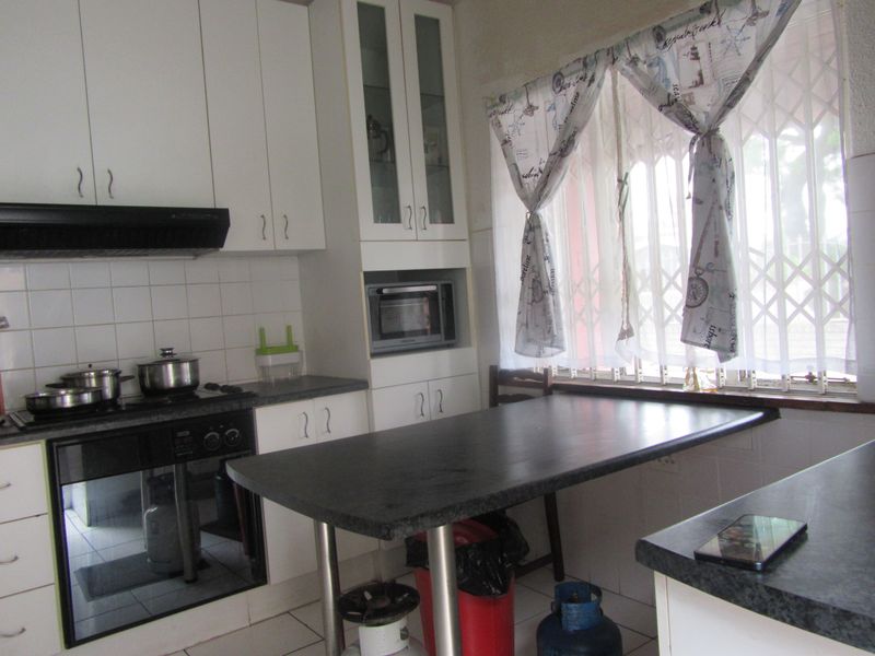 A functional kitchen featuring white built-in cabinetry, dark laminate countertops, a built-in oven with hob, and a security gate over the window.