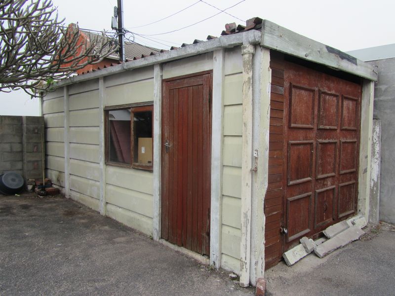 A detached precast concrete garage featuring a timber door and side entrance, showing significant signs of weathering and structural wear.