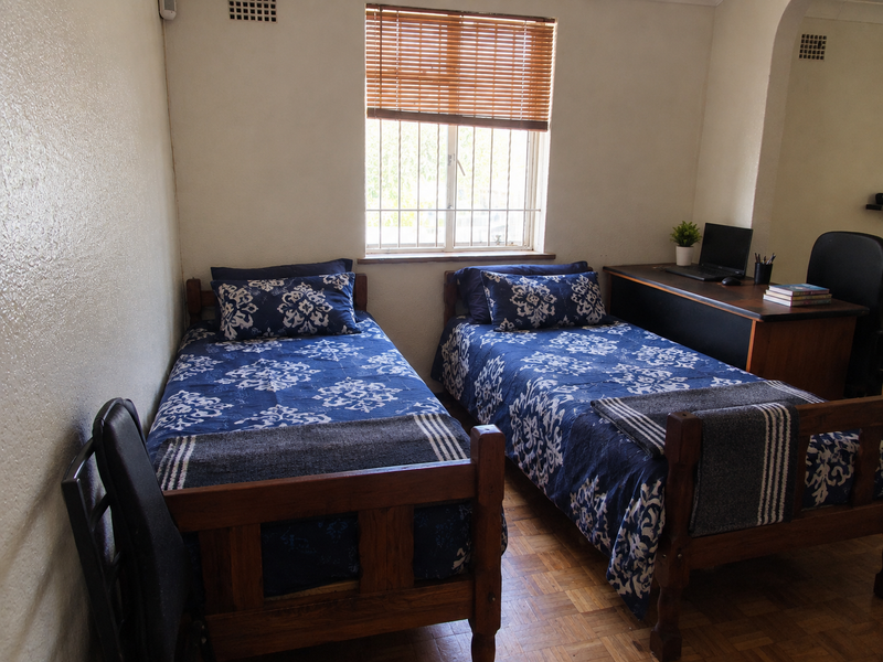 A bedroom featuring parquet flooring, a window with security bars and venetian blinds, and built-in wall ventilation.