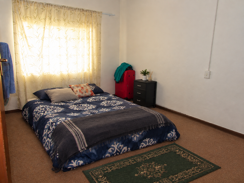 A simple bedroom featuring carpeted flooring and a window with a curtain rail, providing a functional space for rest.