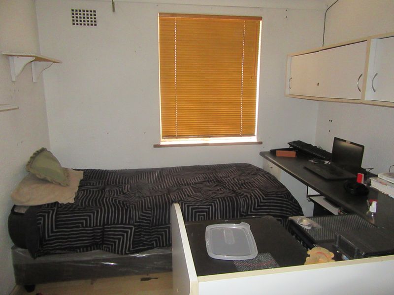 A compact bedroom featuring built-in desk space, overhead storage cabinetry, and wall-mounted shelving, providing functional utility in a modest living area.