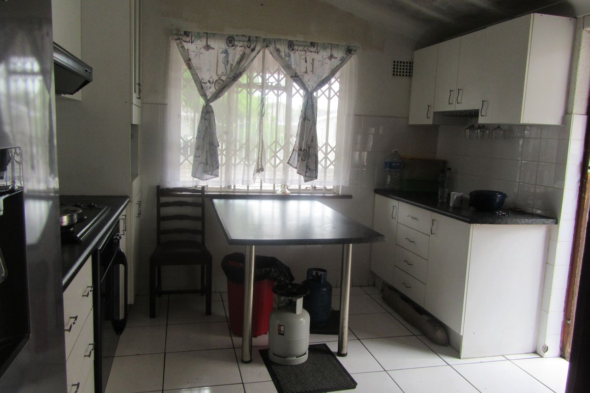 A functional kitchen featuring white built-in cabinetry, dark laminate countertops, tiled flooring, and a window with security bars.