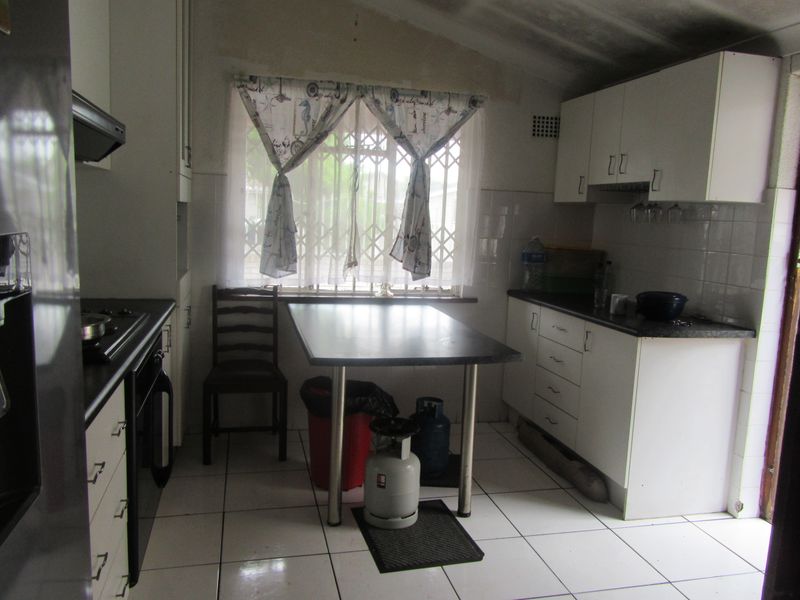 A functional kitchen featuring white built-in cabinetry, dark laminate countertops, tiled flooring, and a window with security bars.