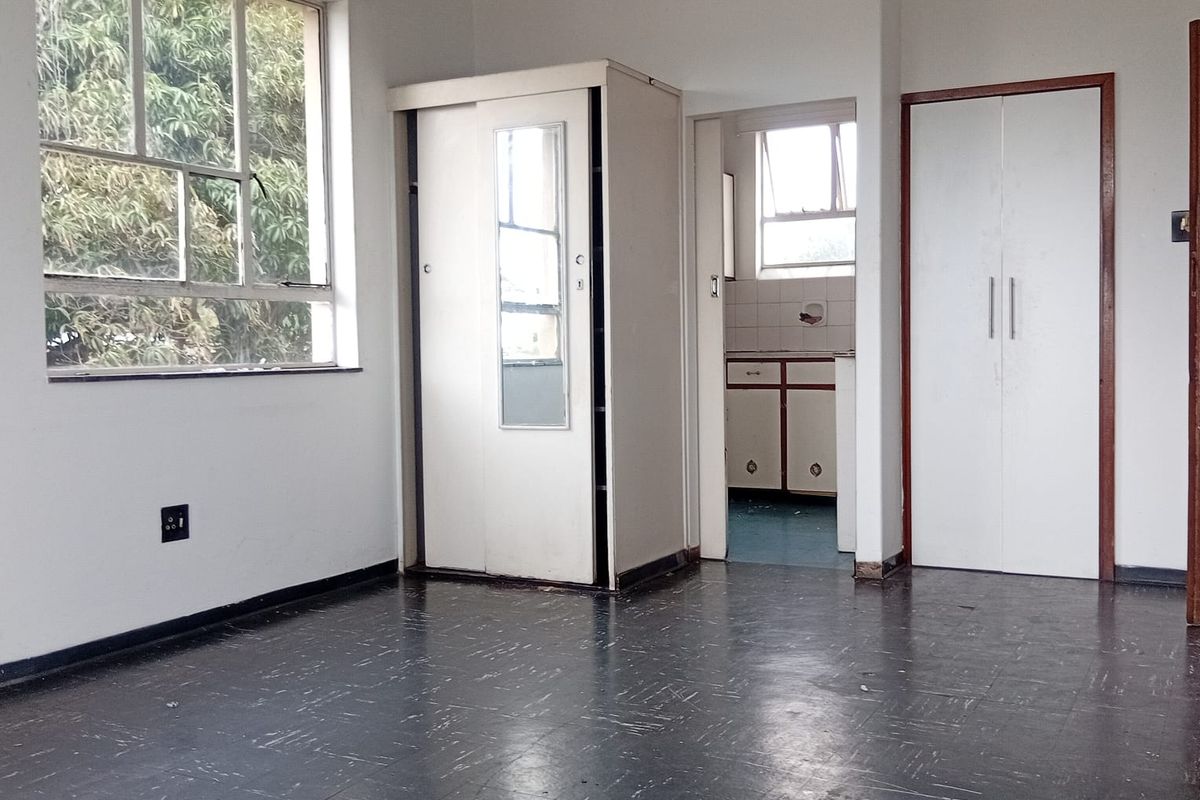 An empty bedroom featuring built-in cupboards, vinyl flooring, and large windows, offering a blank canvas for renovation or interior design updates.