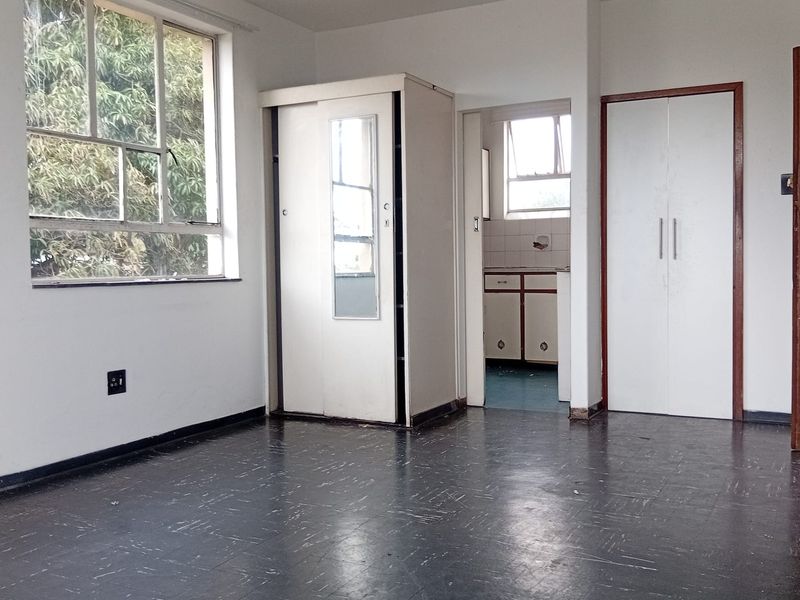 An empty bedroom featuring built-in cupboards, vinyl flooring, and large windows, offering a blank canvas for renovation or interior design updates.