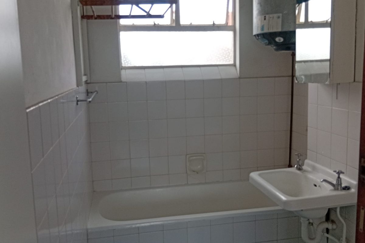 A functional bathroom featuring a bathtub, wall-mounted basin, and tiled walls. The space includes an exposed water heater and requires cosmetic updates.