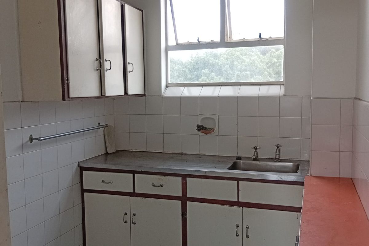 A compact, dated kitchen featuring original built-in cabinetry, a stainless steel sink, and tiled backsplash, offering significant potential for a modern renovation.