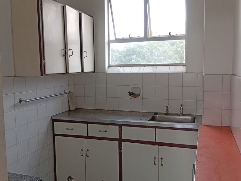 A compact, dated kitchen featuring original built-in cabinetry, a stainless steel sink, and tiled backsplash, offering significant potential for a modern renovation.