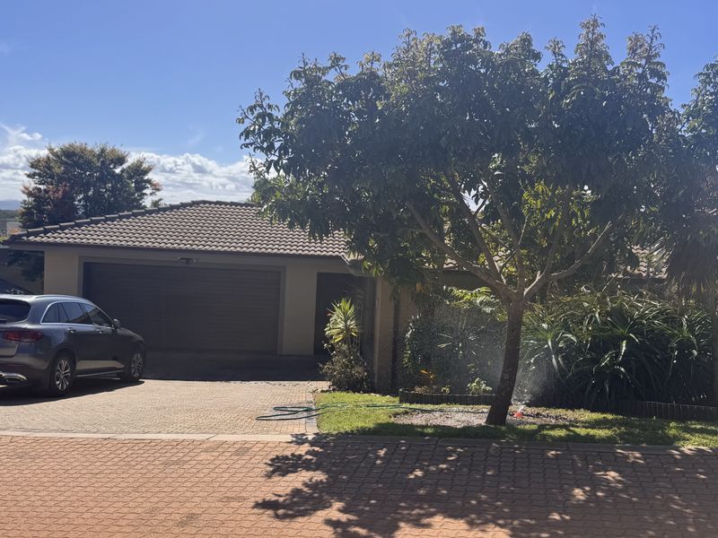 Front view of the property featuring a paved driveway, double garage, and established garden area.