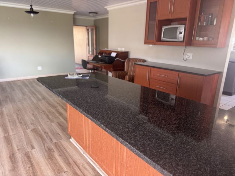 Open plan kitchen area featuring a large granite island, wooden cabinetry, and laminate flooring, seamlessly connecting to the adjacent living space.