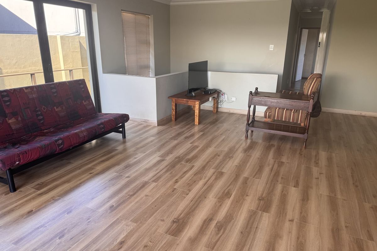 A spacious living area featuring modern laminate flooring, neutral wall tones, and a sliding glass door providing access to the exterior.