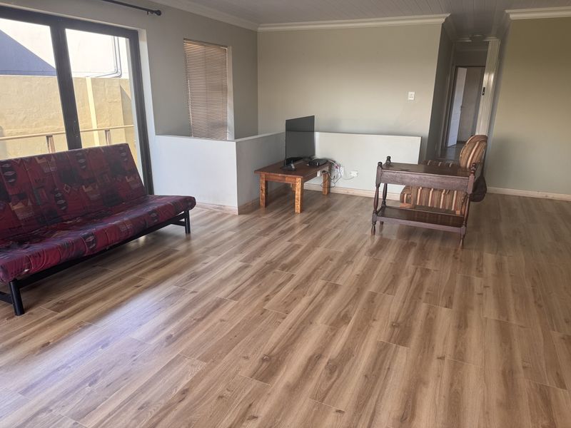 A spacious living area featuring modern laminate flooring, neutral wall tones, and a sliding glass door providing access to the exterior.